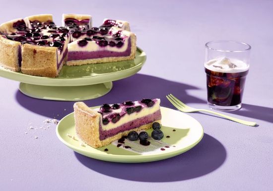 Bild von Creamy Blueberry Cheesecake mit der Beschreibung Vegane Cheesecake-Alternative mit Heidelbeeren, cremig geschichtet auf nussigem Mürbeteig